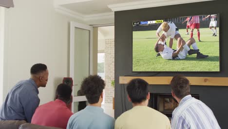 diverse friends supporting and watching tv with diverse male soccer players playing match on screen