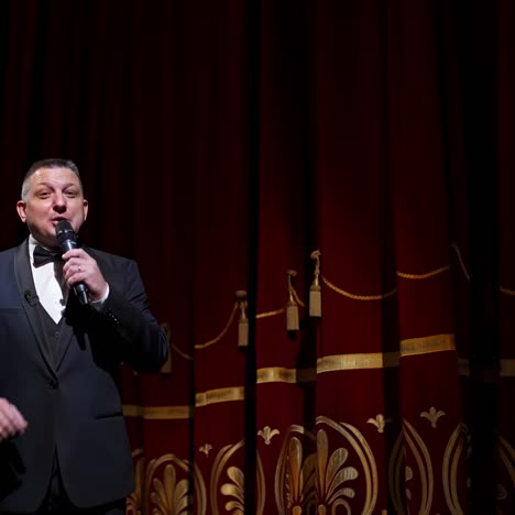 presenter with microphone announces performance before auditorium from stage. theater curtains background