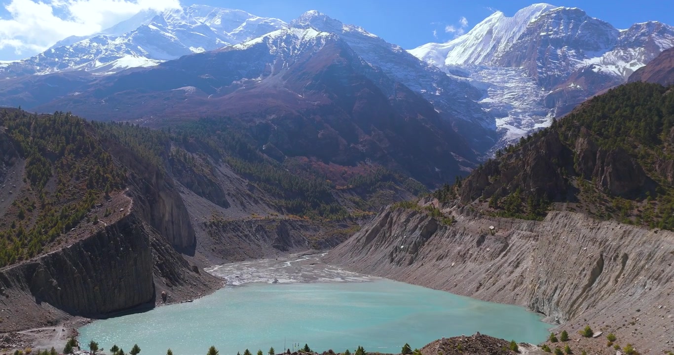 Annapurna Devresi, Manang, Nepal'de, açık güneşli bir günde turkuaz Gangapurna Gölü üzerinde yana doğru süzülen drone çekimi, arka planda karla kaplı Himalaya dağ zirveleri ve bir buzul ile.