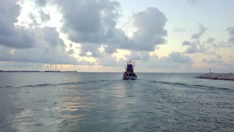 una toma aérea lenta de un dron siguiendo a un barco de pesca que sale de una bahía local y navega hacia el océano abierto durante el amanecer