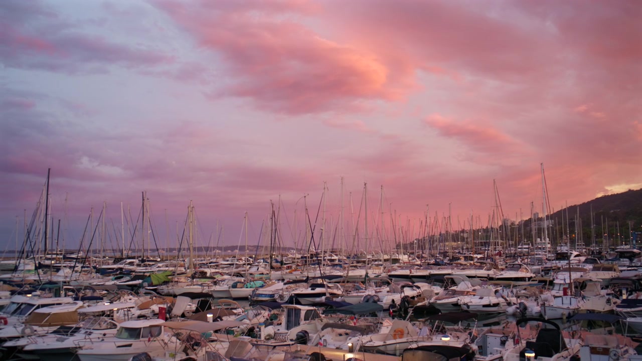 Suggestiva vista serale di yacht e barche a vela riflessi nell'acqua calma della Marina di Port Vauban ad Antibes, Francia, sotto drammatiche nuvole temporalesche.