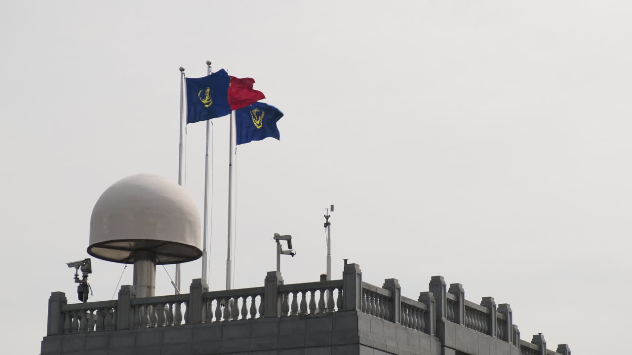 Bandiera nazionale cinese e due bandiere marittime blu che sventolano al vento in cima a un tetto in pietra dotato di un grande radar a cupola bianca e sensori di monitoraggio meteorologico a Shanghai