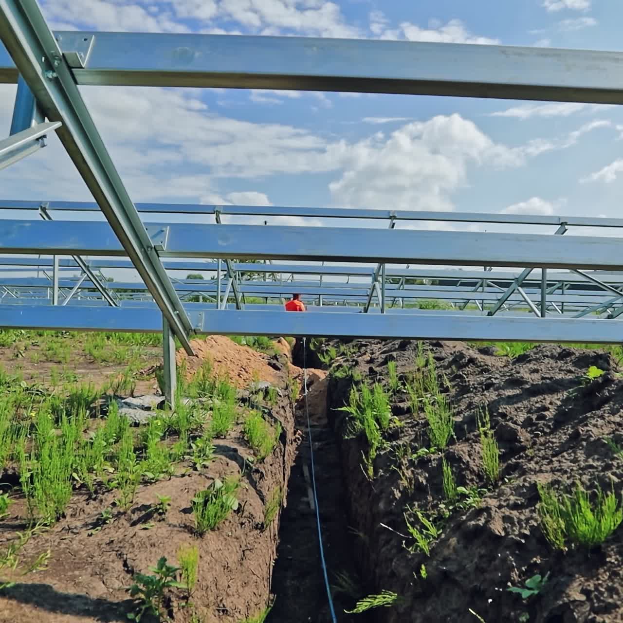 Building of a solar power plant. Worker leads electrical wire on the ground under metal base for future solar panels. Innovative power plant for getting clean energy.