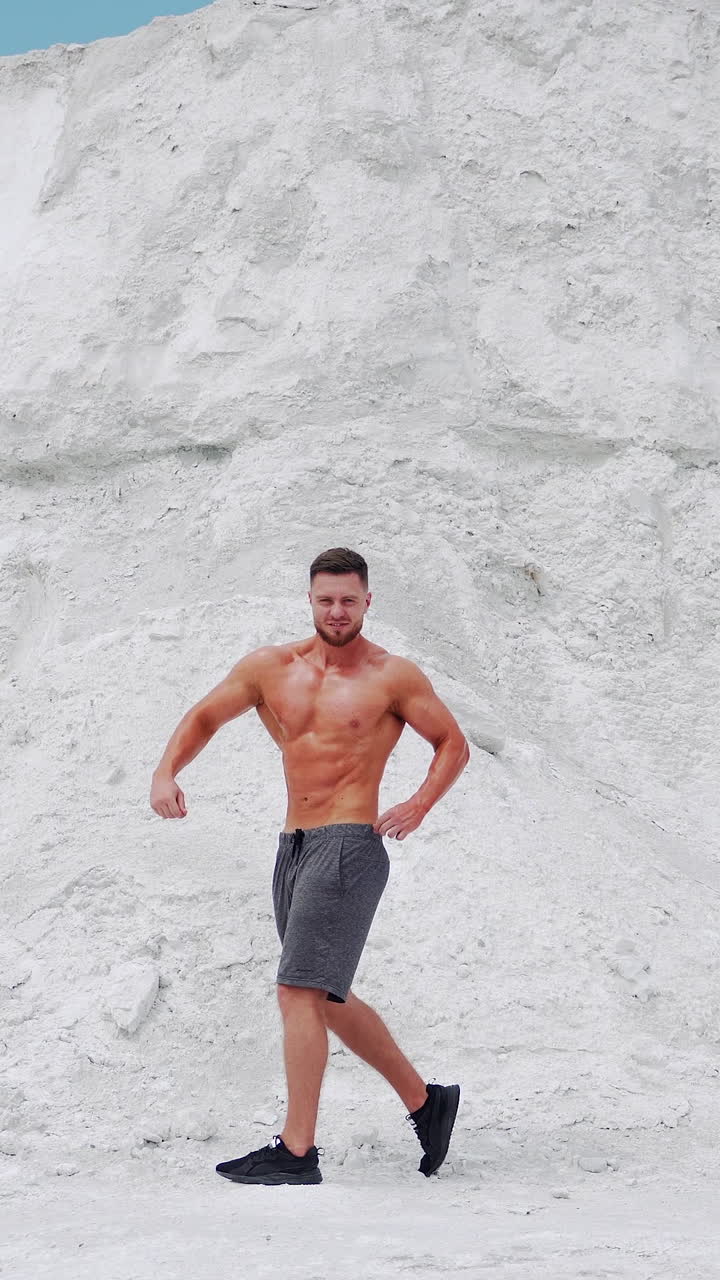 Young bodybuilder poses in nature. Handsome bodybuilder with perfect muscular body posing outdoors. Vertical video