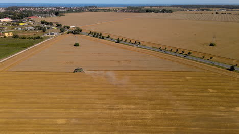 Yellow-grain-fields-as-far-as-eye-can-see-with-combine-harvesting-crops,-drone