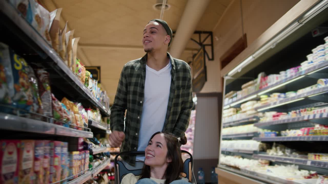 재미있는 젊은 부부, 남자가 여자친구와 함께 쇼핑 카트를 밀고 있습니다.