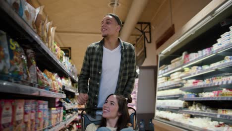 young couple having fun, man pushing shopping cart with his girlfriend inside