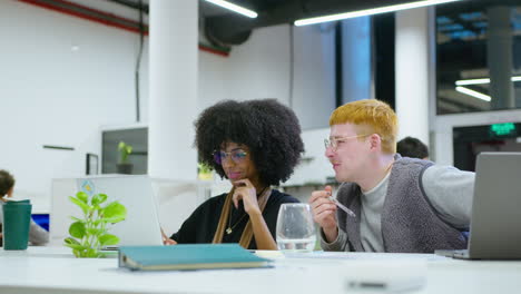 gen z coworkers using laptop and speaking at workplace in the office