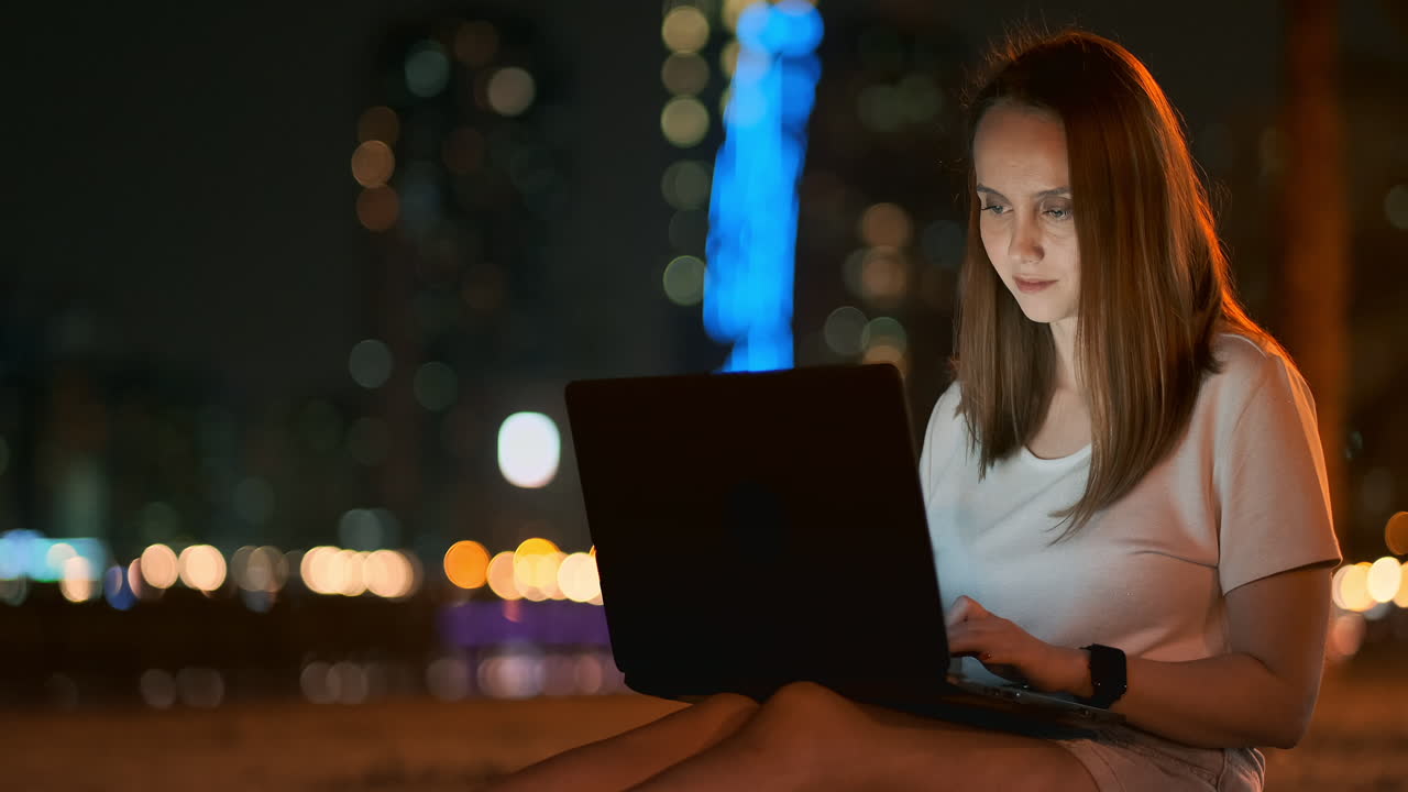 joven diseñadora hermosa trabajando remotamente en una computadora portátil en la calle en el verano bajo palmeras por la noche en el parque de la ciudad. emiratos árabes unidos mujer europea por la noite en dubai
