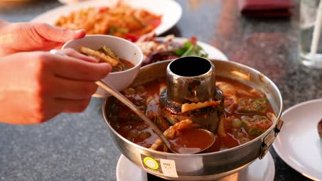 a hand serves soup from a hot pot