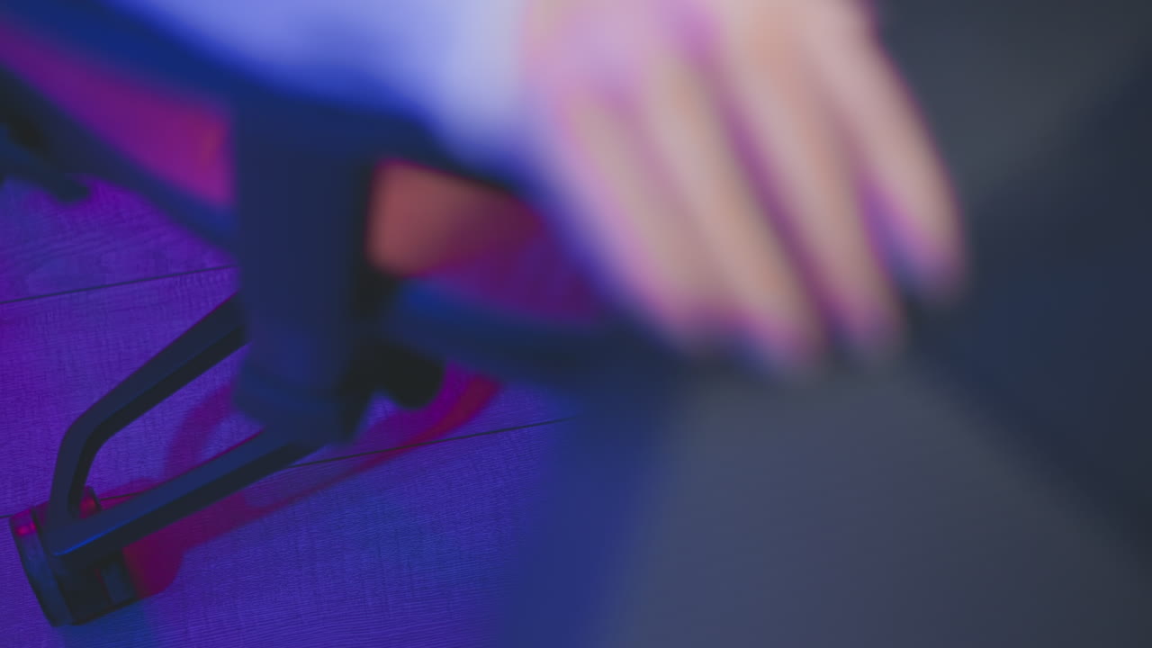 Close up of person wearing fishnet pantyhose sitting down and adjusting rolling seat closer to desk under soft purple and pink neon lighting inside cozy modern studio with gaming setup and table