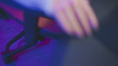 close up of person wearing fishnet pantyhose sitting down and adjusting rolling seat closer to desk under soft purple and pink neon lighting inside cozy modern studio with gaming setup and table