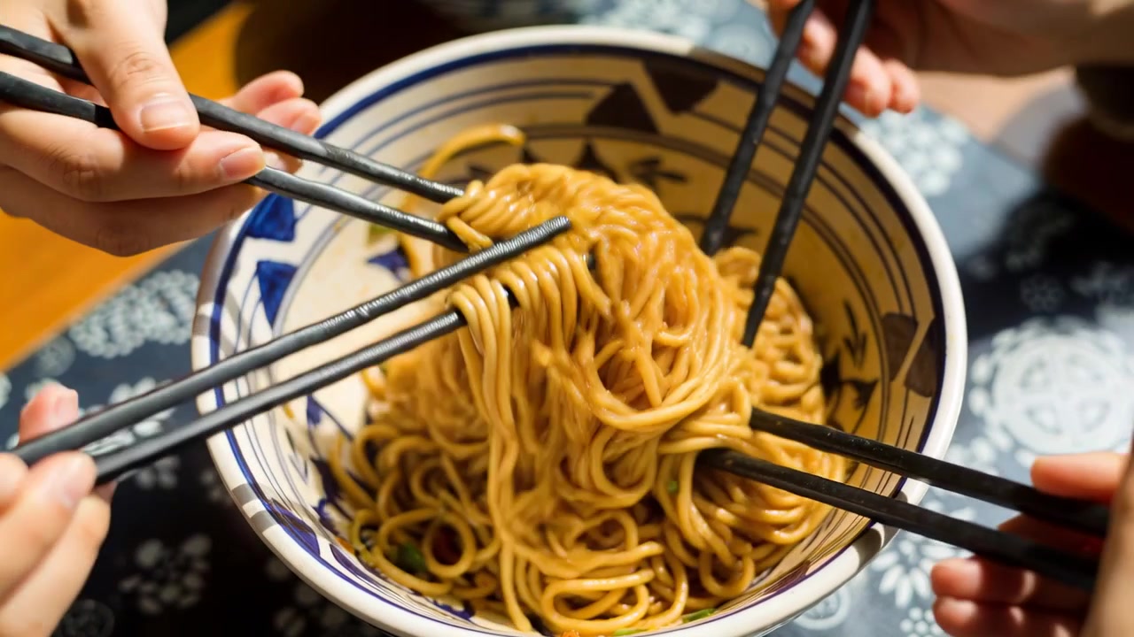 Braccia che si allungano nelle maniche, avvolgendo spaghetti conditi a casa, condividendo con una ciotola blu e bacchette nere.