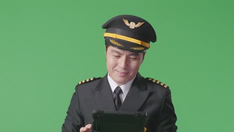 close up of asian man pilot using a tablet while standing in the green screen background studio