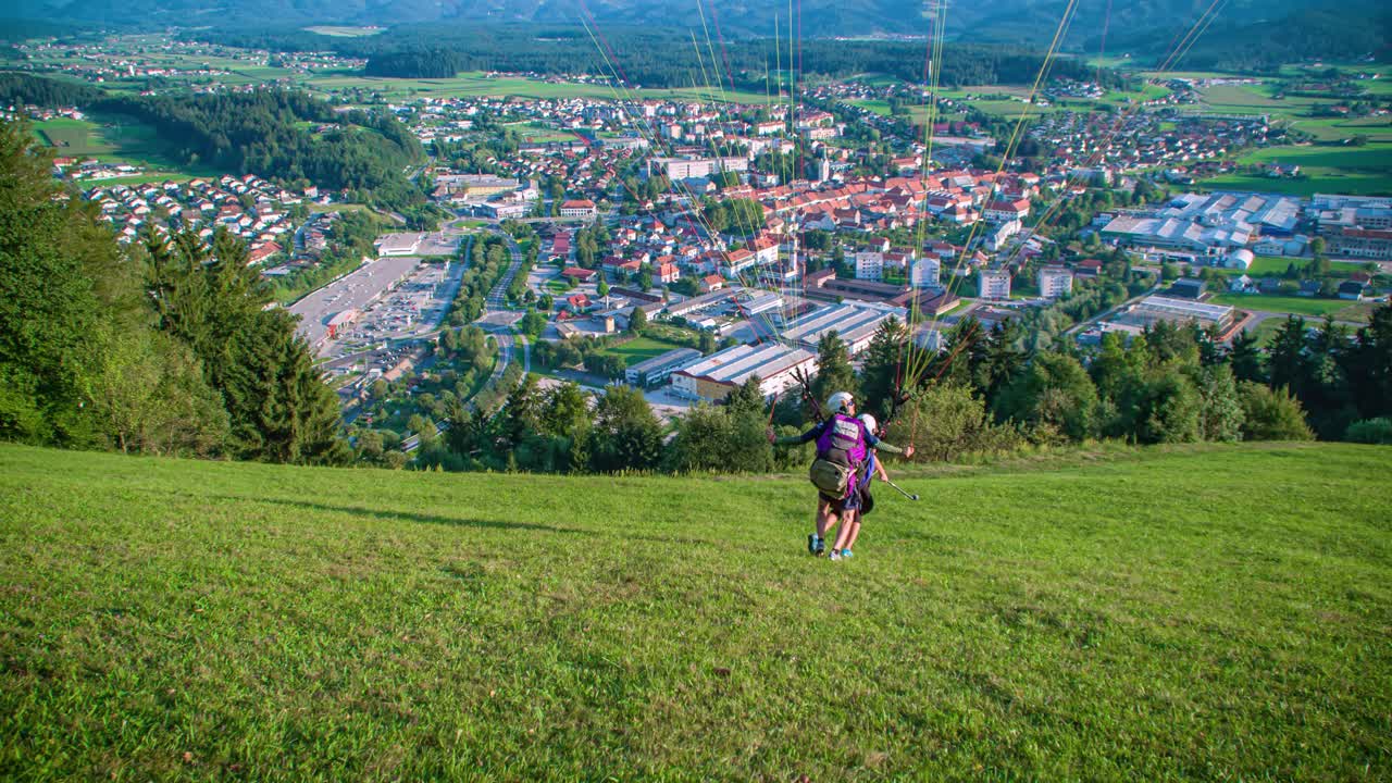 Paragliding instructor and his client or student are preparing for a tandem flight and taking off, flying away from the camera