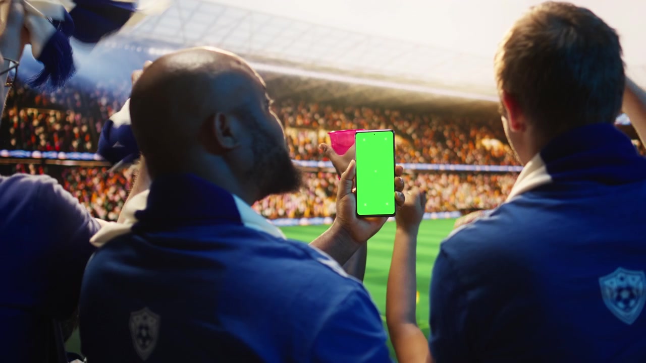 Primo piano di un telefono con schermo verde usato da un uomo in uno stadio affollato