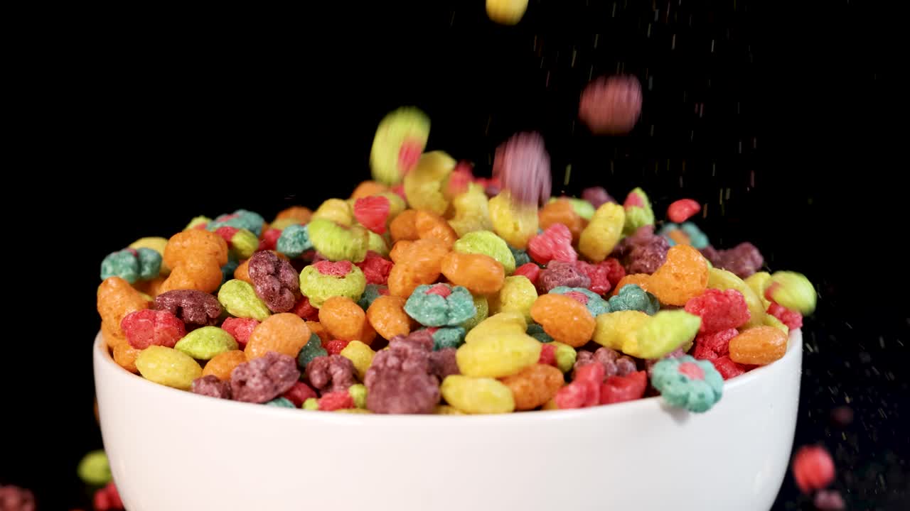 Vibrant cereal pieces cascade into a white bowl against a black background, creating a dynamic and colorful scene