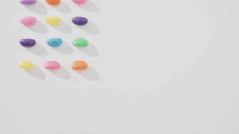 video of overhead view of rows of multi coloured sweets with copy space over white background