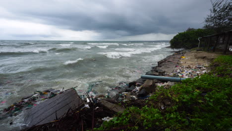 strong waves crash against damaged coastal wall with surrounding ocean trash and pollution