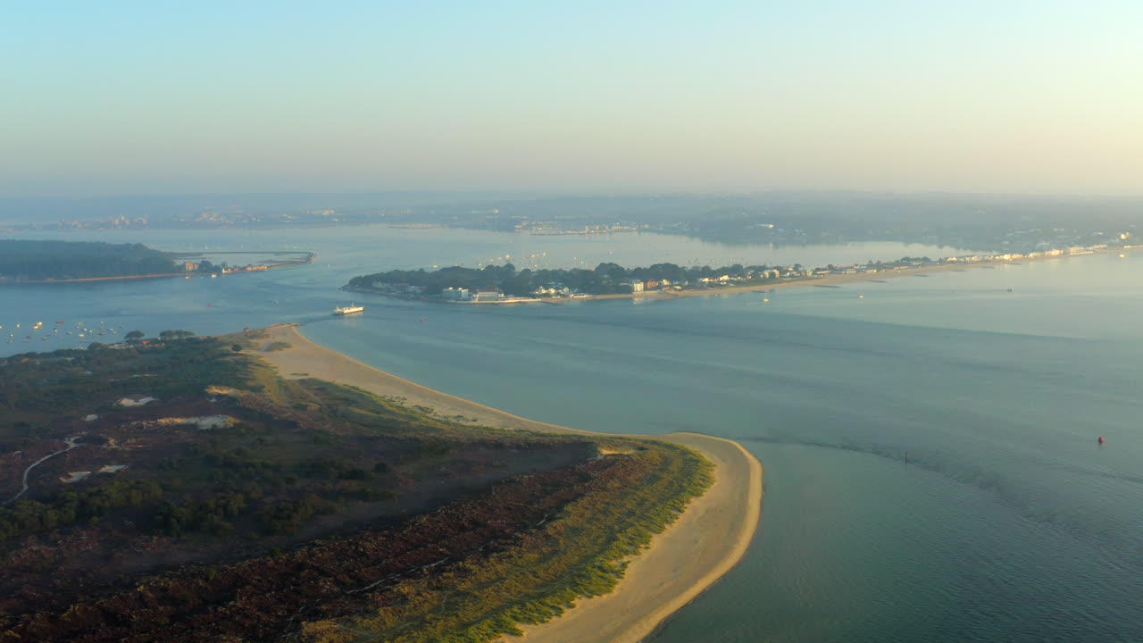 Uma tomada aérea panorâmica do Porto de Poole, Sandbanks, Ilha Brownsea e praia de Studland na hora dourada com mar calmo e tranquilo