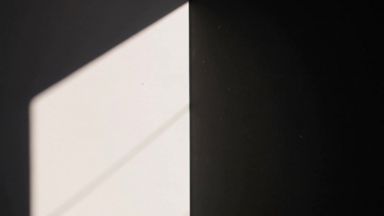 Entering sunlight creating rectangular patch on wall, casting diagonal shadow over seam and dust