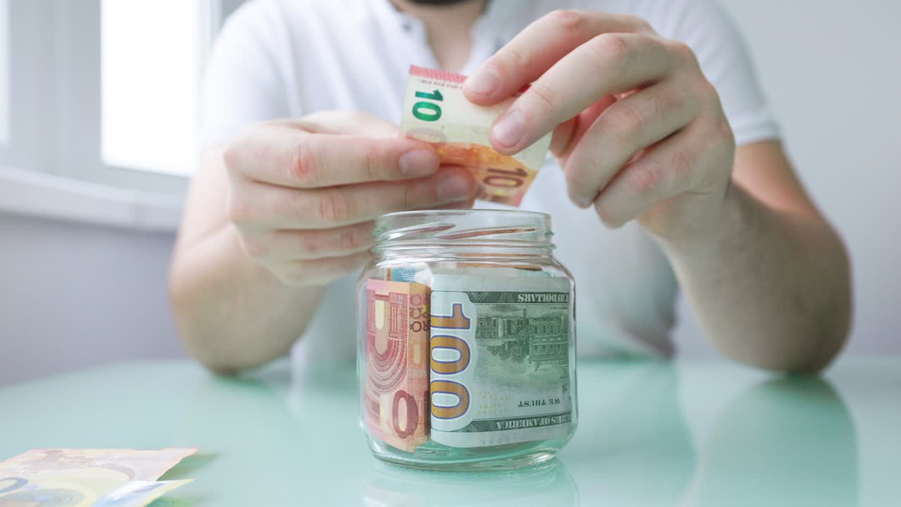 Beskåret billede af mandlig hånd, der lægger euroseddel i glaskrukke