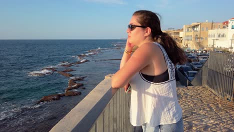 a woman is standing on a pier overlooking the acre old city, israel.