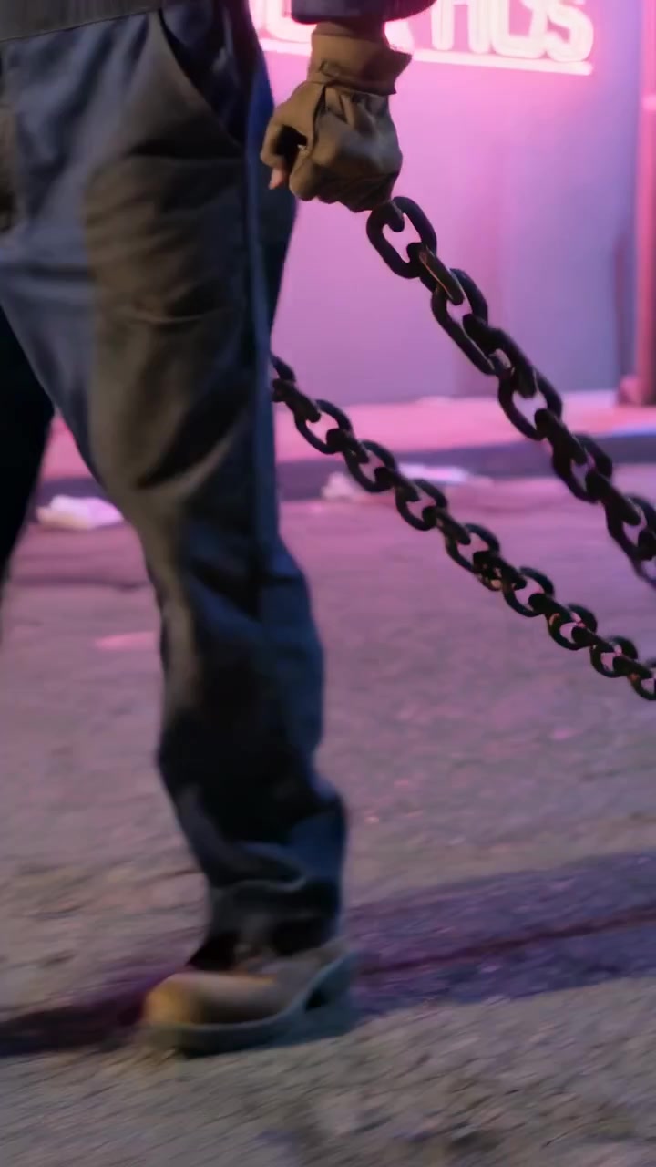 Vertical video: Stepping worker with gloves pulling chains toward curb on neon sidewalk, copy space