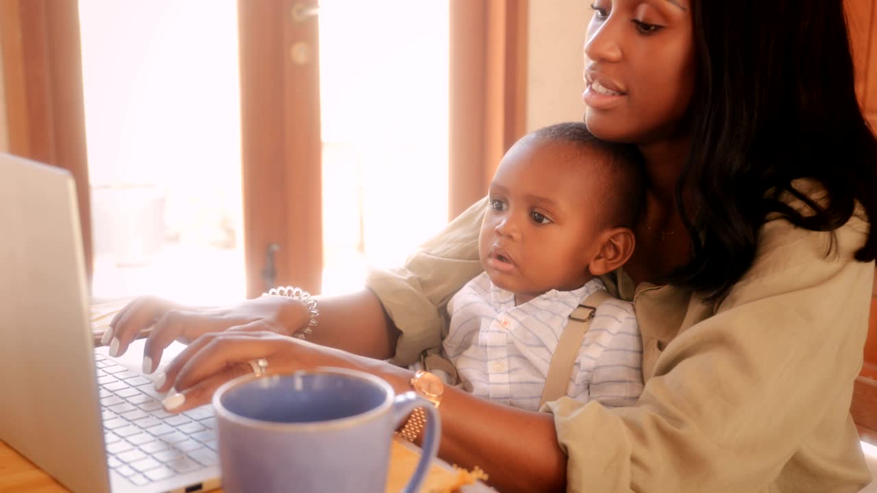 Blogger mother with baby boy working from home on laptop