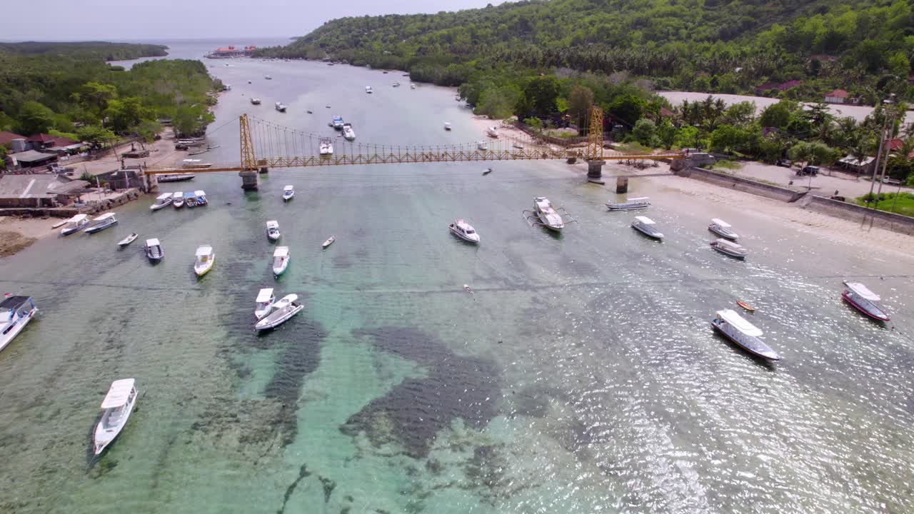 Ponte giallo brillante che attraversa acque basse soggette a maree, collegando le isole di Nusa Lembongan con barche ancorate, ripresa aerea.