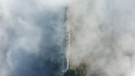 Mountainous-cliff-disappears-into-thick-heavenly-mist,-top-down-aerial