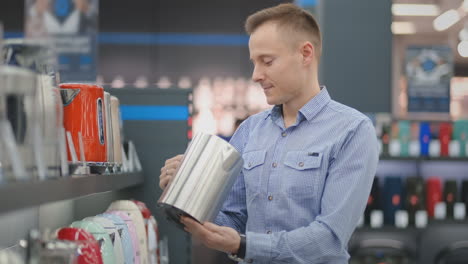 young man chooses electric kettle for his new home in appliances store