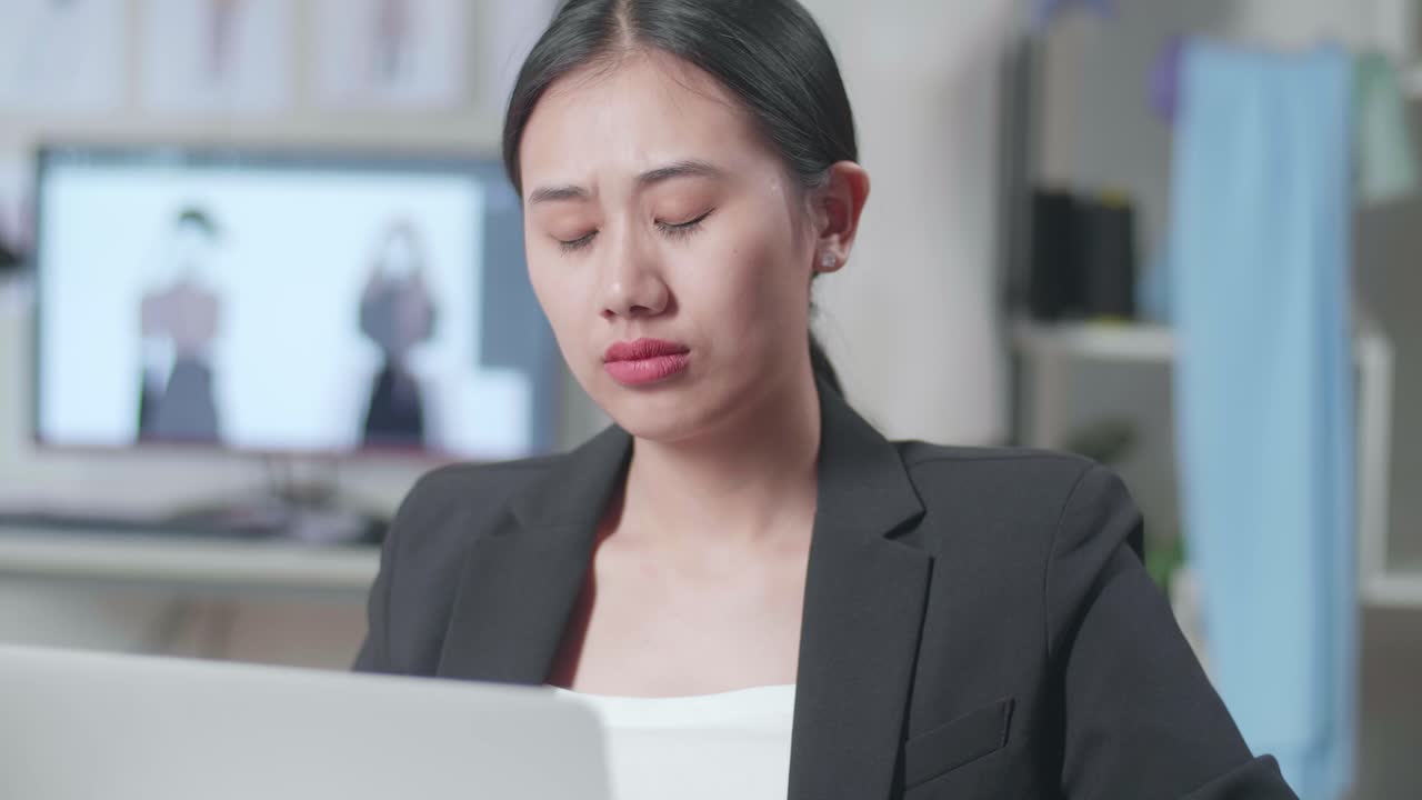 비즈니스 슈트를 입은 아시아 여성 디자이너가 노트북에서 일하고 스튜디오에서 옷을 디자인하는 동안 생각하고 있습니다.