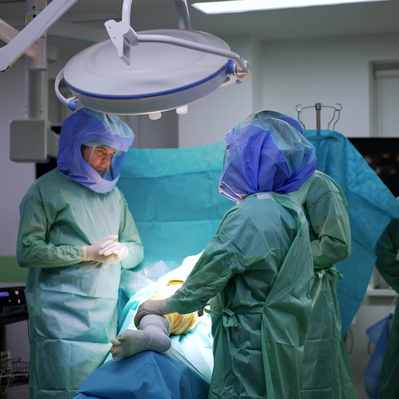 Three doctors wearing protective suits and helmets stand over the patient. Surgeons deciding on the strategy of operation on leg