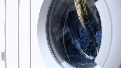 the laundry is washed in a white automatic washing machine behind a glass door, the metal drum rotates in different directions in turn. washing clothes jeans. homework 4k