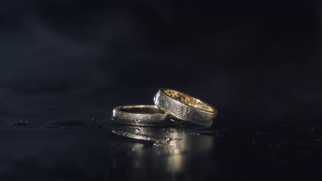anillos de bodas en la superficie del agua oscura brillando con la luz. macro de primer plano