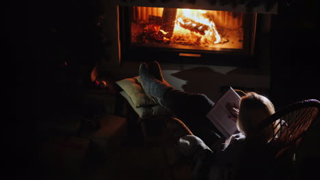 young woman reads a book while sitting by the fireplace