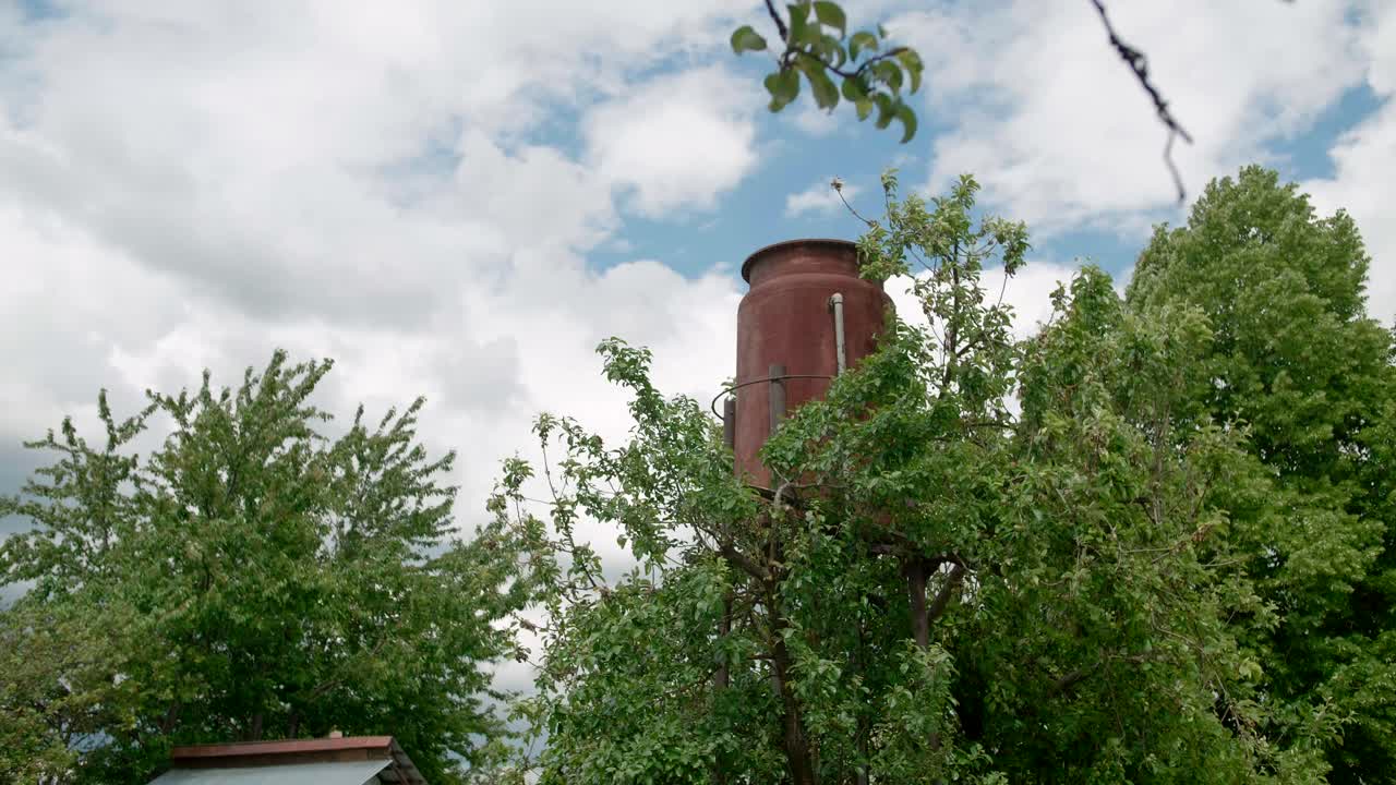 torre de agua vieja y oxidada escondiéndose detrás de las copas de los árboles