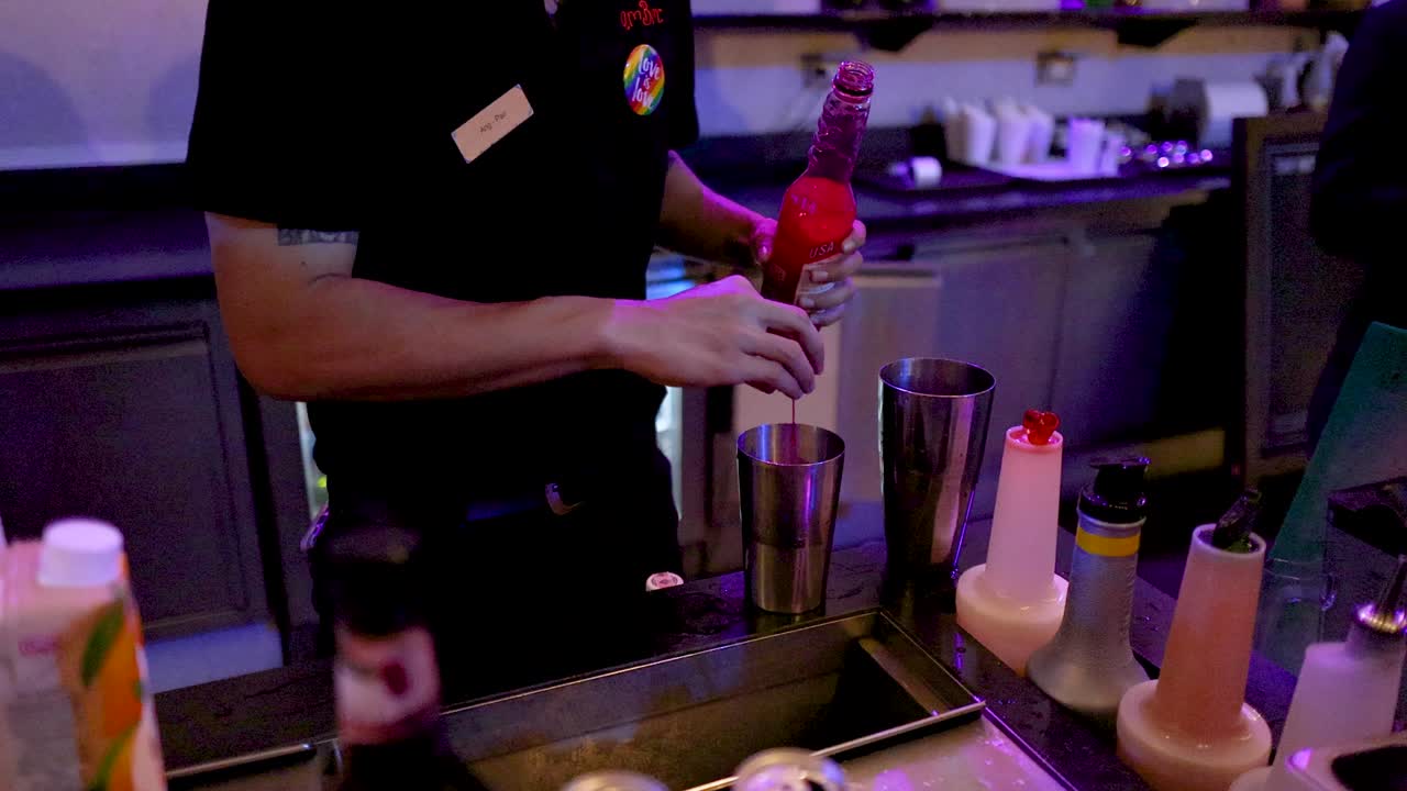 Bartender prepares vibrant cocktail using syrup and shaker in dimly lit Bangkok nightlife bar