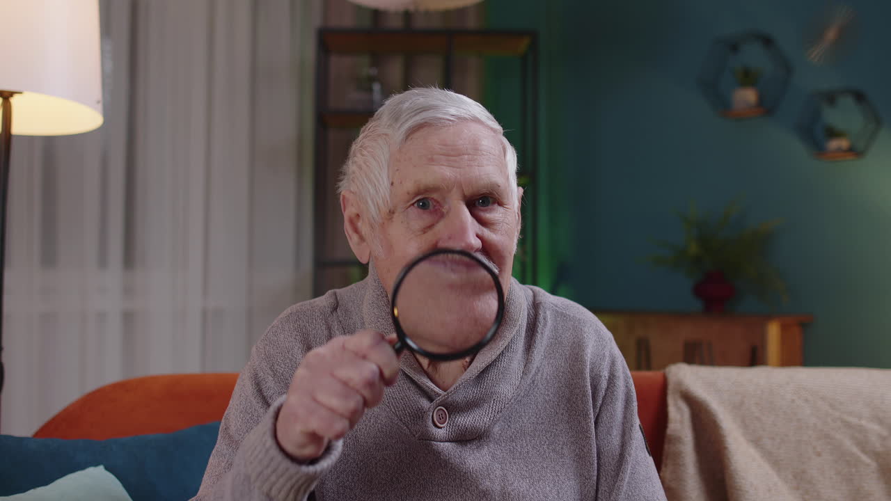 abuelo anciano mirando a través de una lupa, leyendo, investigando, examinando en casa