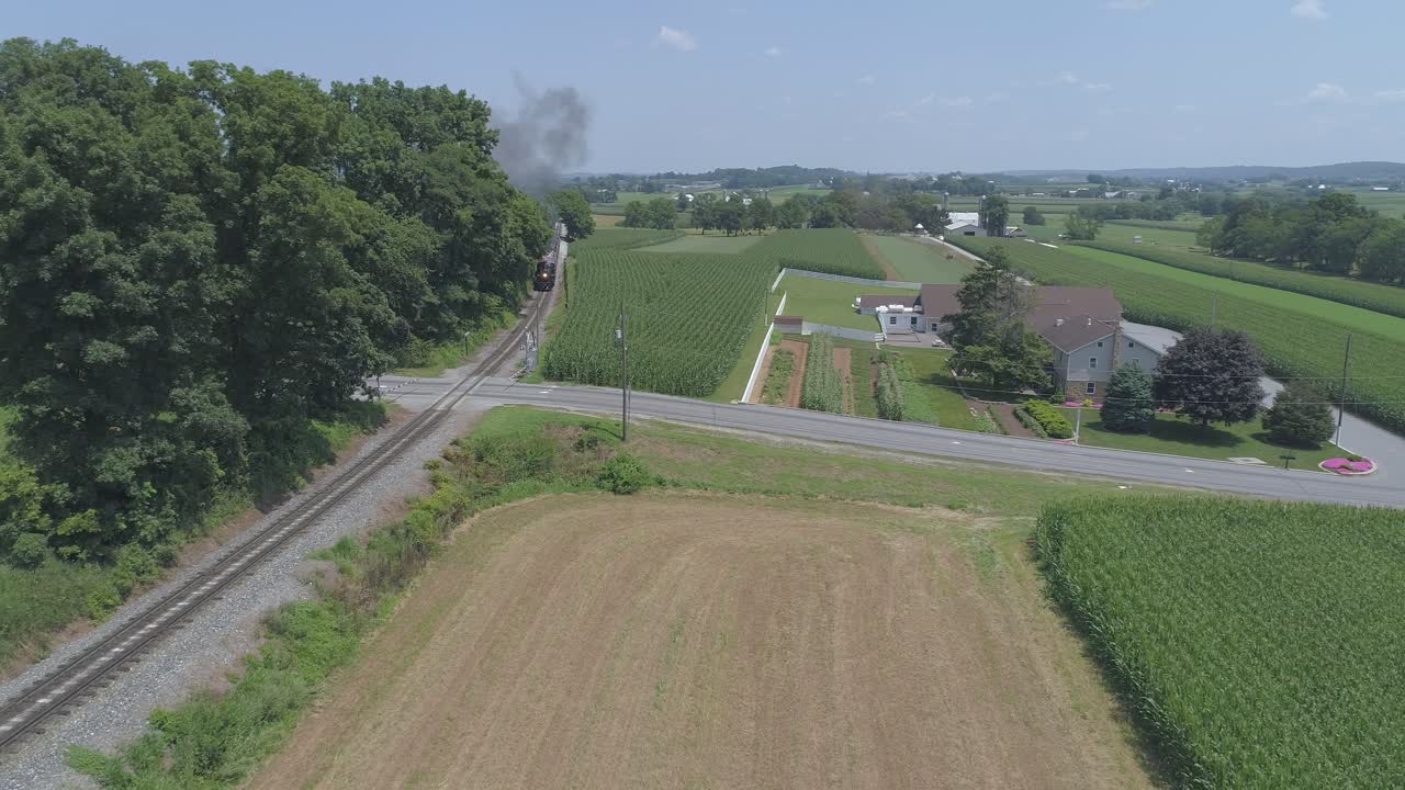 вид с воздуха на паровоз 1910 года с пассажирским поездом, пыхтящий дымом, путешествующий по амишской сельской местности в солнечный летний день, как видно с беспилотника