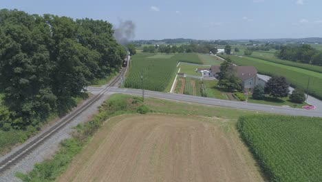 Aerial-View-of-a-1910-Steam-Engine-with-Passenger-Train-Puffing-Smoke-Traveling-Along-the-Amish-Countryside-on-a-Sunny-Summer-Day-as-Seen-by-a-Drone