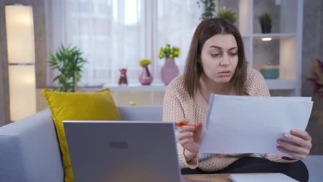 mujer joven preocupada que trabaja en una computadora portátil, mirando documentos y papeleo.