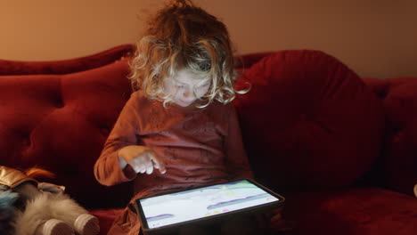una niña pequeña juega o mira una tableta con la luz de la pantalla en una habitación oscura