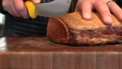 person slicing whole piece of back bacon into thick delicious slices, slider shot