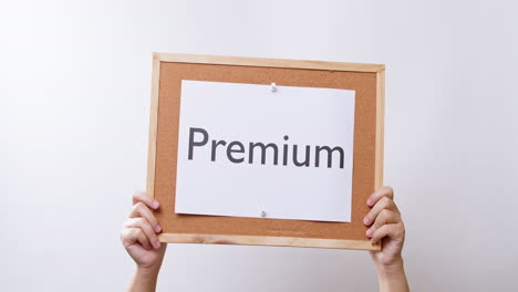 woman's hand shows the paper on board with the word premium in white studio background with copy space