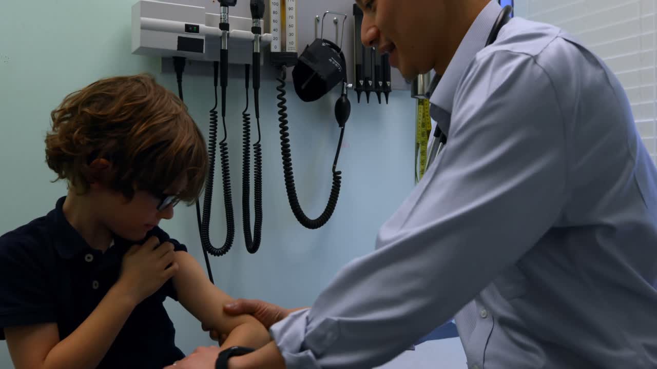 Side view of young asian male doctor injecting syringe to caucasian boy patient in clinic 4k