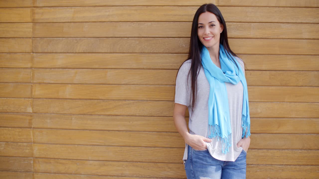 나무 벽 근처에 주머니에 손을 가진 웃는 여자