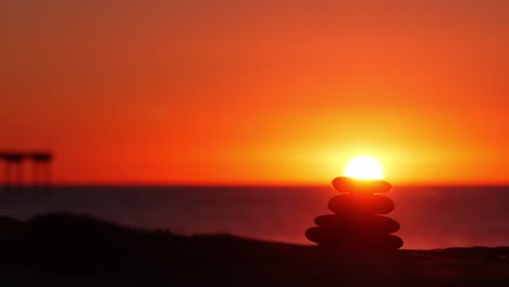 una pila de piedras de guijarros, una playa de arena, un cielo al atardecer, una roca equilibrada por el agua.
