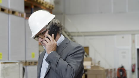 supervisor enfocado en anteojos y casco hablando por teléfono en fábrica